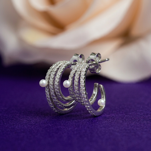 Silver hoop earrings with pearls on a purple surface, blurred rose in the background