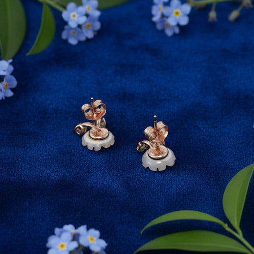 Pair of earrings on a blue fabric background with flowers and leaves.