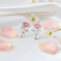 Floral-themed earrings with pink flowers and clear stones on a white surface with pink petals.