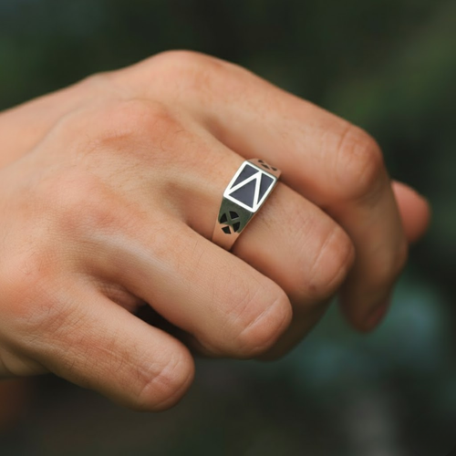 Close-up of a hand wearing a ring with a geometric design on a blurred background