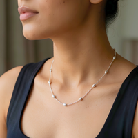 A close-up lifestyle shot of a model wearing a delicate silver necklace with small, evenly spaced silver beads on a chain.