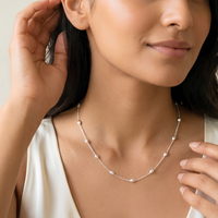 A close-up lifestyle shot of a woman wearing a delicate silver necklace with small, evenly spaced round beads on a light cream satin top.