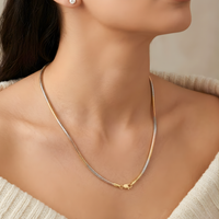 A close-up of a woman's neck and upper chest wearing a delicate two-tone chain necklace with a gold and silver finish, paired with a white knit sweater.