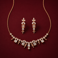 A gold-tone jewelry set featuring a necklace and matching drop earrings, embellished with clear baguette and round-cut stones, displayed on a deep burgundy background.
