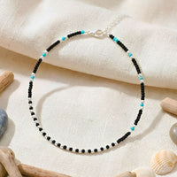 Beaded bracelet with black and turquoise beads on a textured beige surface with seashells and driftwood.