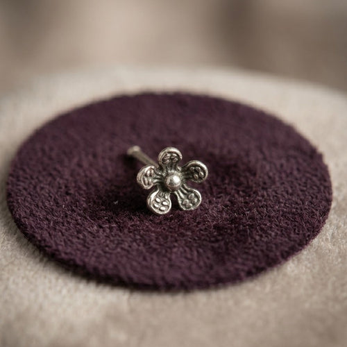 Silver flower-shaped earring on a purple cushion with a blurred background