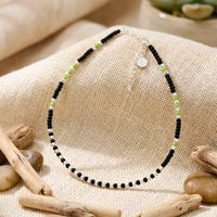 anklet with black and green beads on a textured surface with wooden elements