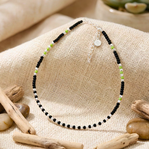 anklet with black and green beads on a textured surface with wooden elements