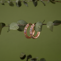 Rose gold hoop earrings with colorful gemstones on a branch with green leaves.
