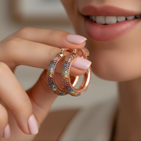 Rose gold hoop earrings with colorful accents held by a hand against a neutral background