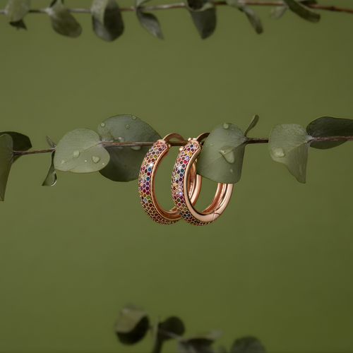 Rose gold hoop earrings with colorful gemstones on a branch with green leaves.