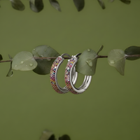 Silver hoop earrings with colorful gemstones on a green leafy background