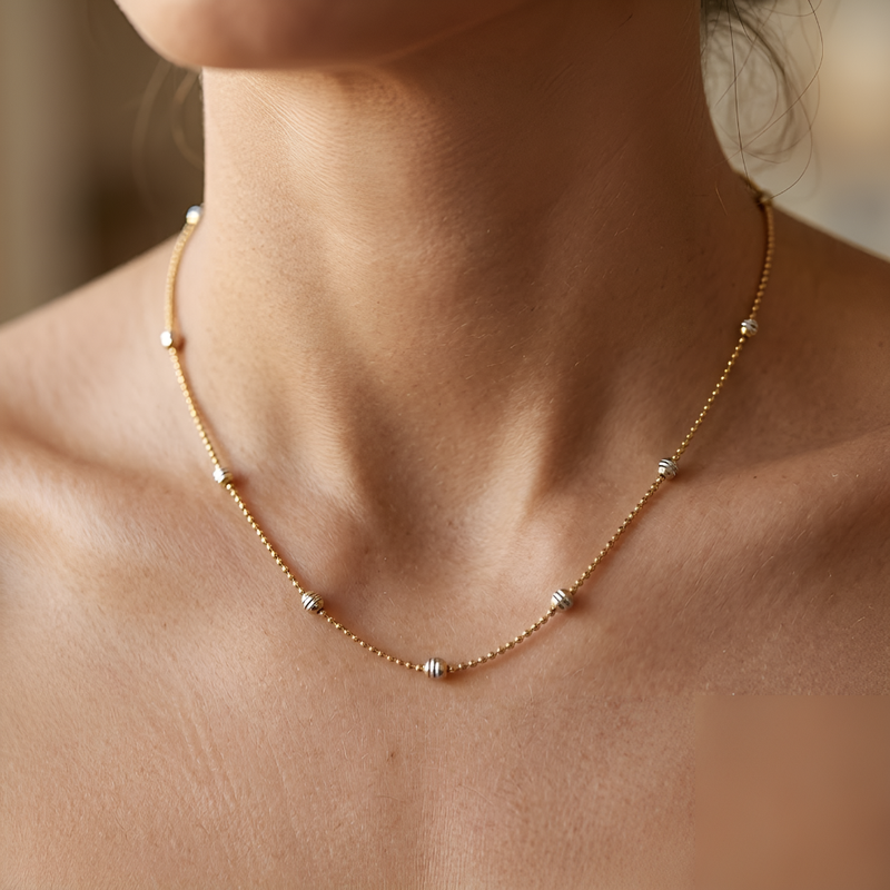A delicate gold chain necklace with small silver-toned bead accents, shown worn on a model's neck.