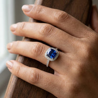 Hand wearing a ring with a blue gemstone on a neutral background